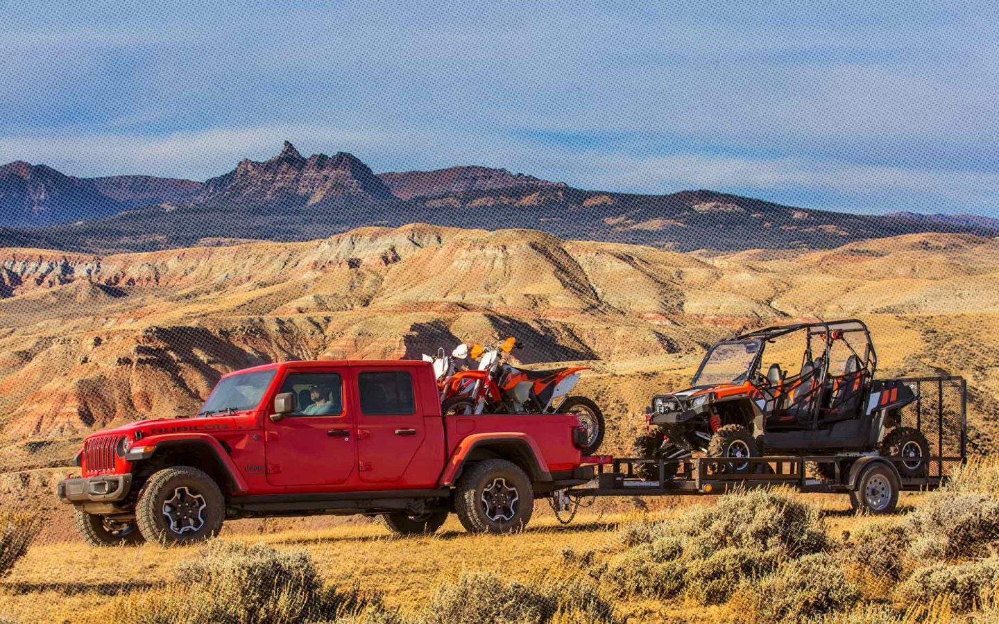 Red Gladiator with dirt bikes in truck bed towing an offroad vehicle