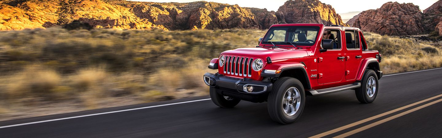 A gray 2020 Jeep® Wrangler Unlimited Sahara parked on a rocky trail with trees and hills in the background.