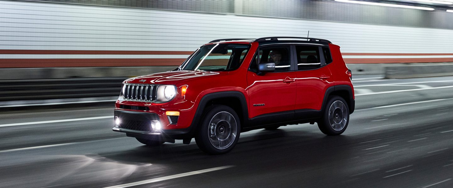A red 2021 Jeep Renegade being driven through a tunnel with headlamps lit.