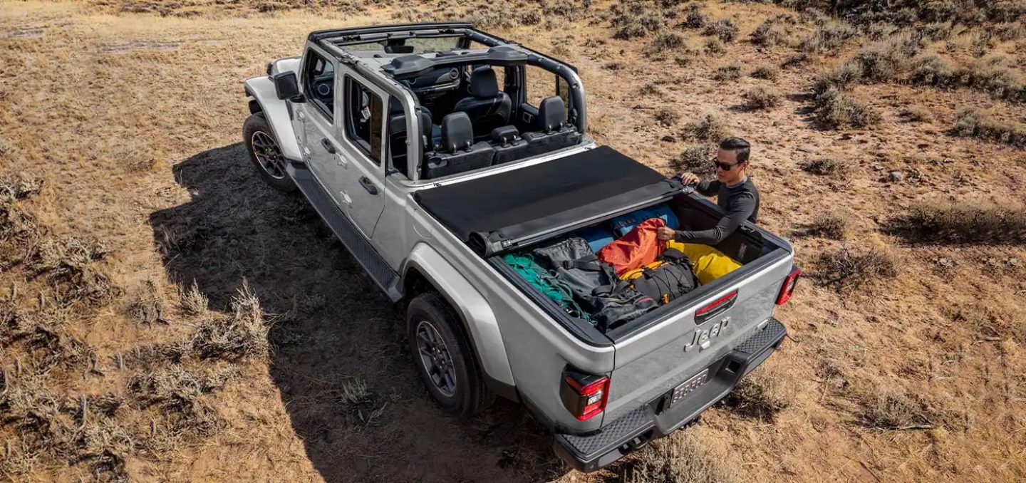 A 2022 Jeep Gladiator Rubicon towing two jet skis as it is driven along a beach near the water.