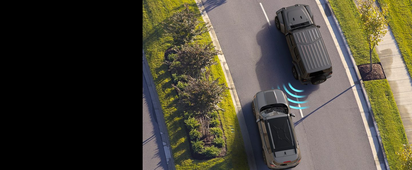 The 2022 Jeep Wrangler Sahara with illustrated sensor bars emanating from the rear of the vehicle, intersecting an approaching vehicle in the next lane.