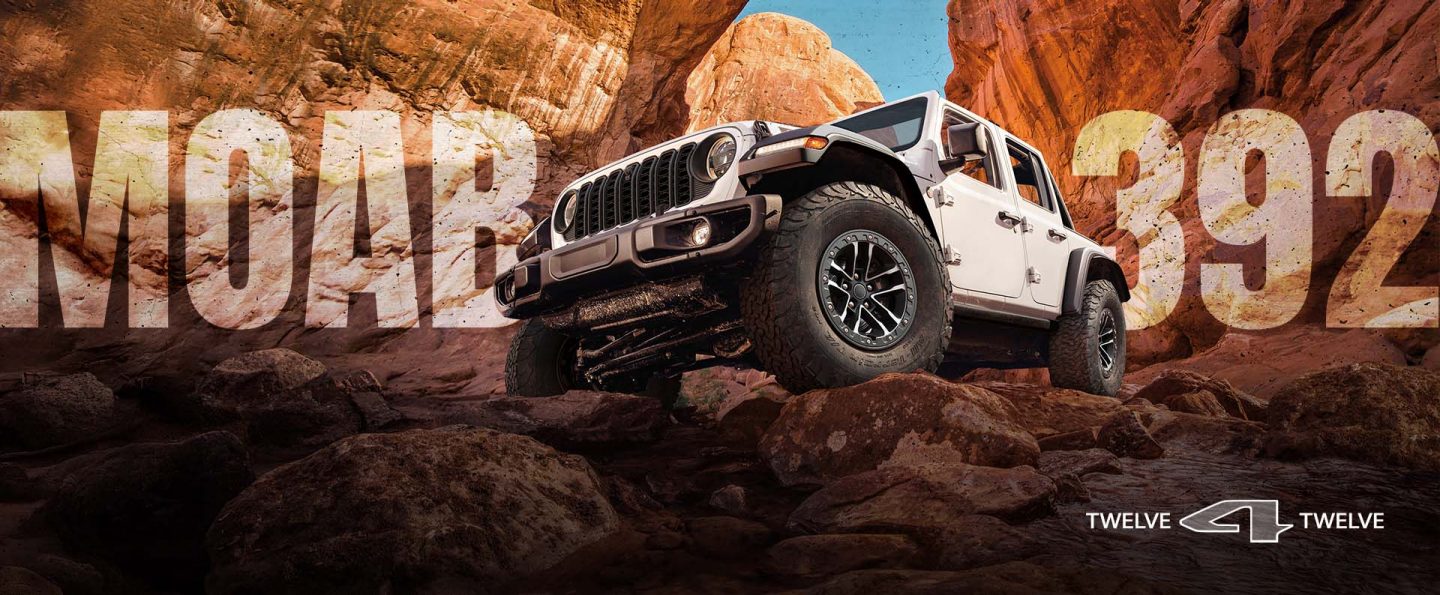 A white 2026 Jeep Wrangler Moab 392 crawling over boulders, surrounded by huge rock formations. Moab 392. 12 for 12.